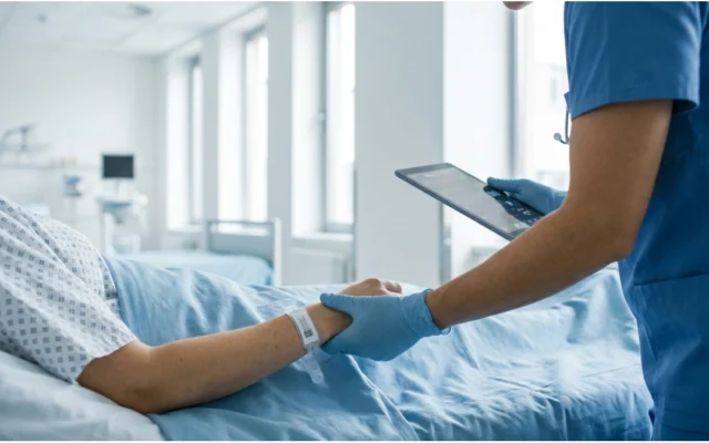 Healthcare professional checks the identification wristband of a hospitalized patient in a hospital bed.